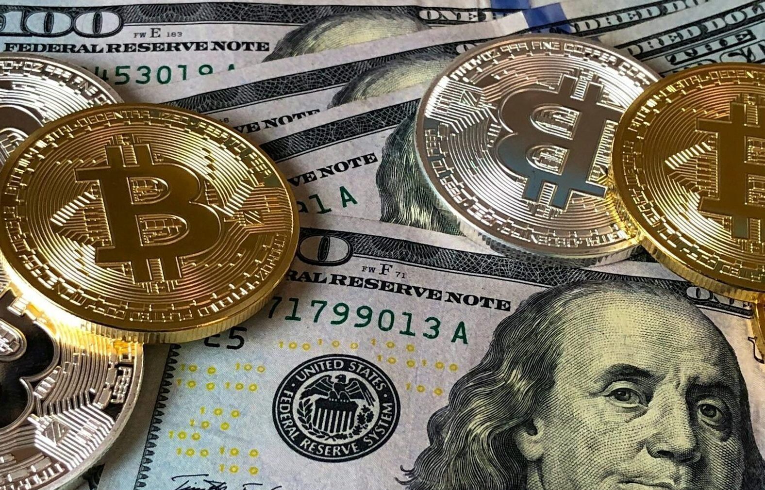 A close-up photo depicting Bitcoin coins on top of US dollar bills, symbolizing finance and cryptocurrency.